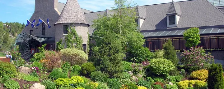 Le Casino de Charlevoix à La Malbaie, un bâtiment au toit gris avec une tourelle ronde, derrière des jardins de rocaille aménagés