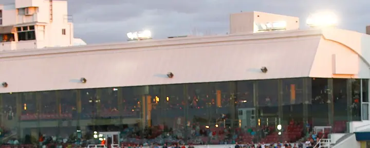 La tribune vitrée de l'Hippodrome de Trois-Rivières, avec des spectateurs le long de la clôture, au crépuscule