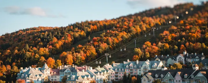 Un village de villégiature aux façades pastel au pied d'une pente de ski aux couleurs d'automne, avec une ligne de télécabine